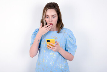 young caucasian woman wearing blue T-shirt over white background being deeply surprised, stares at...