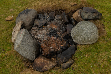 The remains of a burnt out camp fire out in the countryside. ashes and charcoal are surrounded by rocks that would stop the from spreading and becoming unsafe 