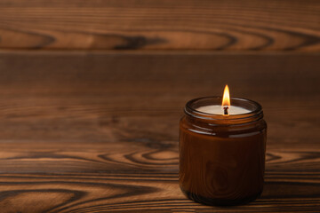 Obraz na płótnie Canvas Cozy burning candle in brown glass jar on brown texture wood.winter home decor.Soy ecological candle.Home and interior decoration.Place for text.Space for copy.