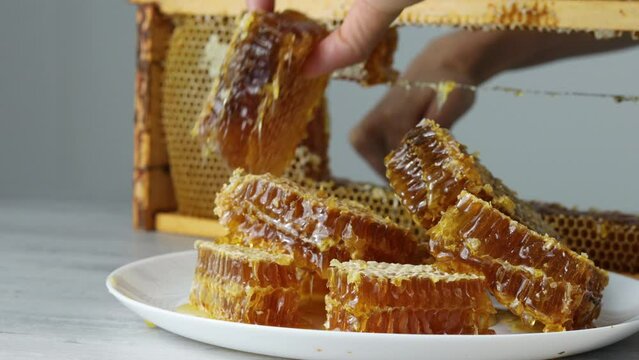 Cutting of piece of honey from open honeycomb in wooden frame on the table