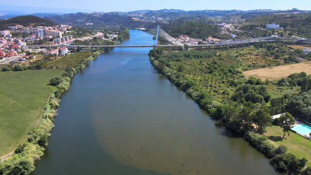 A camera drone flies over Mondego River towards the Rainha Santa Isabel Bridge (Portuguese: Ponte Rainha Santa Isabel) in Coimbra, Portugal
