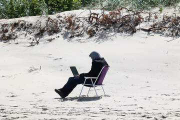 Człowiek pracuje zdalnie on line na laptopie na plaży.  - obrazy, fototapety, plakaty