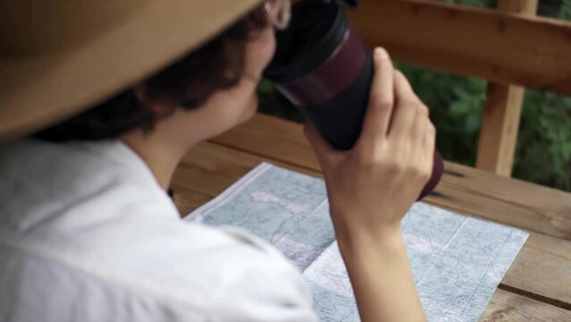 A calm, peaceful girl tourist drinks hot tea from a thermos cup sitting in a fox in a gazebo at wooden table tourist on the background of the map drinks tea from a thermos cup Hiking alone with nature