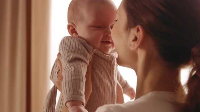 Shooting of mother and baby. Happy young woman holding newborn in her arms and kisses him. Cute child smiling and laughing. Home, family, maternity