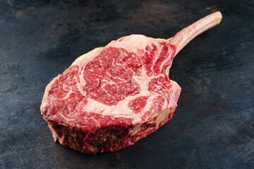 Raw dry aged wagyu tomahawk steak offered as close-up on an old black rustic board with copy space