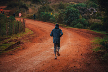 Obraz premium Morning run in Kenya. A woman trains on the road with red soils and prepares for a race. Training camp in the city of Iten in East Africa