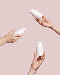 Hands holding blank white plastic tubes on pink background. Packaging for pills or capsules. Medic...