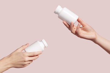 Hands holding blank white plastic tubes on pink background. Packaging for pills, capsules or...