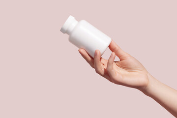Female hand holding blank white squeeze bottle plastic tube on pink background. Packaging for...