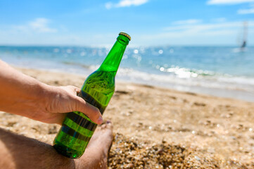 A bottle of beer in a man's hand on the beach. Sea holiday concept.
