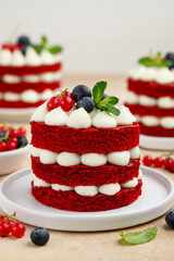 Mini red velvet cakes decorated with berries and mint. Portion cake on a white plate with....