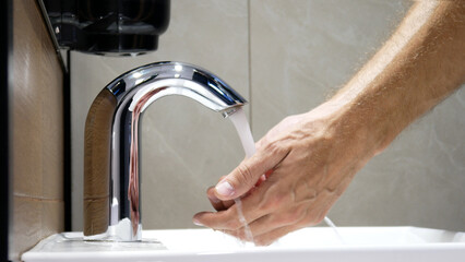 A man washes his hands using a touchless faucet close-up - obrazy, fototapety, plakaty