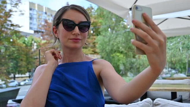 Woman wearing blue summer dress and sunglasses taking selfie photos at a restaurant