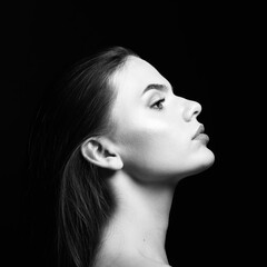 Beauty, make-up and fashion concept. Young and beautiful woman with long dark hair profile view portrait. Model looking aside the camera in black studio background. Black and white image