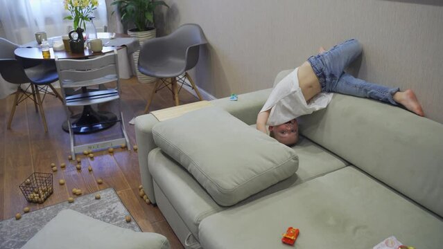 Cute child messing around at home in kitchen, lying on couch, throwing things, making disorder. Childhood and parenthood. 4K