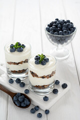 Dessert with cottage cheese, fresh blueberries and granola in a glass on a white wooden background.