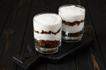Greek yogurt with granola on a wooden dark wooden background.