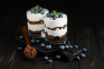Dessert with cottage cheese, fresh blueberries and granola in a glass on rustic background.