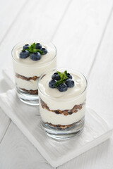 Dessert with cottage cheese, fresh blueberries and granola in a glass on a white wooden background.