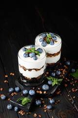 Dessert with cottage cheese, fresh blueberries and granola in a glass on rustic background.
