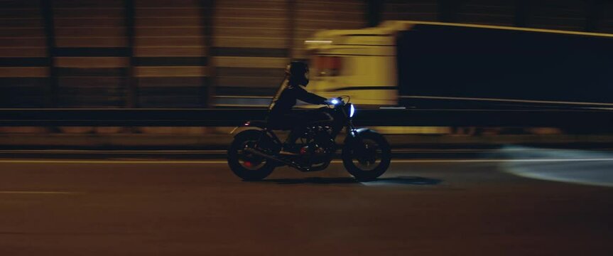 TRACKING Shot of a biker riding his custom built cafe racer motorcycle through city at night. Shot with 2x anamorphic lens