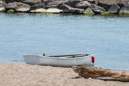 White painted wooden row boat with oars in the oar locks drawn up on the sand of Toronto's Balmy Beach at midday.