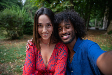 Selfie of two people, a male and a female sitting on a bench in a park. Smiling couple or friends.