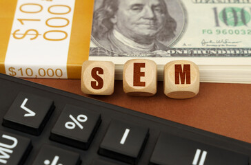 On the table are dollars, a calculator and cubes with the inscription - SEM