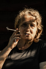 Portrait of elderly woman with cigarette close-up on natural background. Sunset light on face of senior. High quality photo