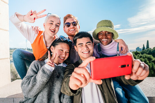 Five multiracial friends taking a photo with a mobile phone posing in front of the camera and smiling.