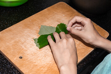 The boy is learning to cook. A child wraps minced meat in a grape leaf for making dolma