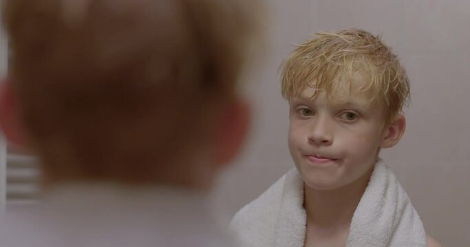 Teenage boy critically examines himself in the mirror. Portrait of preteen child in the bathroom. Self-esteem gives children confidence.