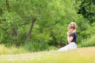 Young woman praying in a grassy field