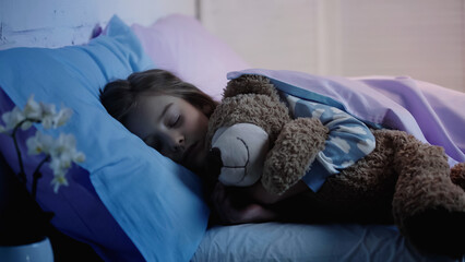 Preteen kid hugging soft toy while sleeping on bed at home.