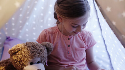 Smiling child looking away near soft toy in wigwam in evening. © LIGHTFIELD STUDIOS