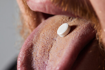 Man taking pill, mouth open with tongue sticking out.