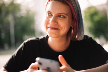 Happy young woman smiling looking away holding smart phone outdoors