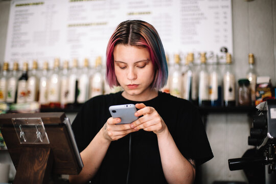 Female barista using smart phone at checkout counter in coffee shop