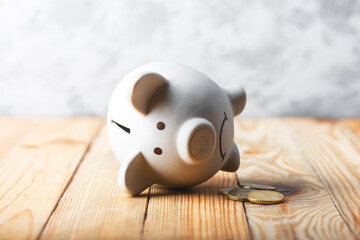 A sad piggy bank behind stack of euro coins symbolizing the fall of monetary assets. White moneybox...