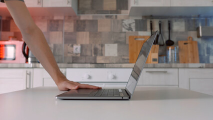 Close up side view of hands open up new laptop with black keyboard on kitchen background. Action....