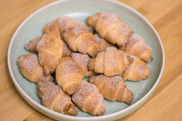 Homemade croissants bagels with sugar powder on blue plate in bowl on wooden table bakery fresh tasty food