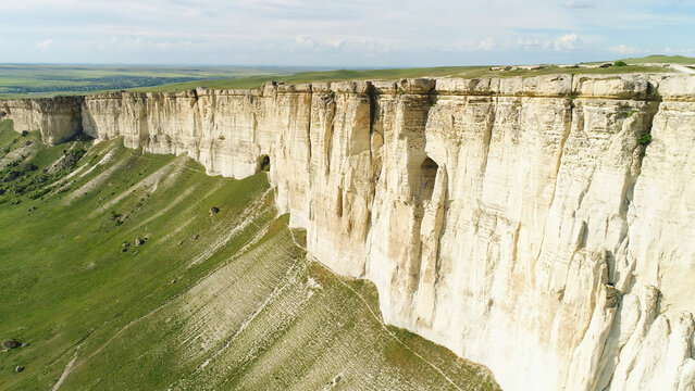 Stunning landscape of White Rock in Crimea with bright green meadow at the foot. Shot. Aerial for the beautiful mountain with flat top and green field on cloudy sky background.