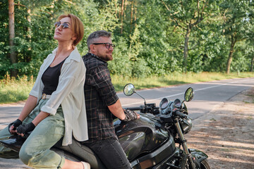 Fototapeta na wymiar Middle age couple talking and having fun, sitting on a motorcycle, traveling together on a forest road