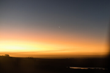 sunset in the mountains with a crescent moon with dam in the foreground