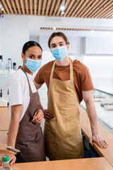 Interracial sellers in medical masks looking at camera in confectionery.