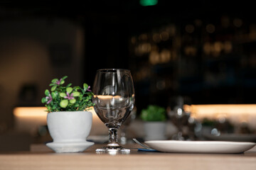 Restaurant table decorated with a small pot with flowers and a bar in the background. Decorated table in a restaurant with clean glass and plate before serving