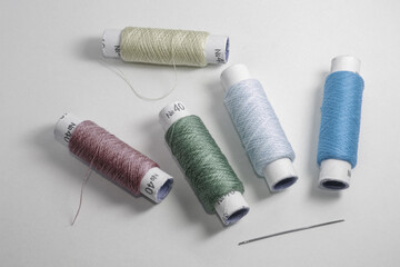 Five rolls with threads of cold colors and one needle on the white background