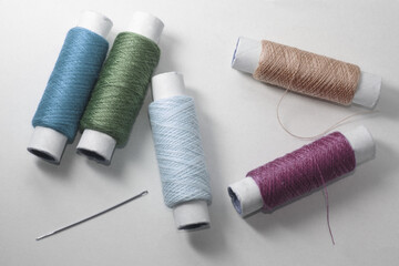 Five rolls with threads of cold colors and one needle on the white background
