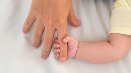Hand of little baby and finger of adult on white sheet bed background