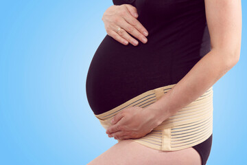 Pregnant woman with elastic maternity band on blue background
